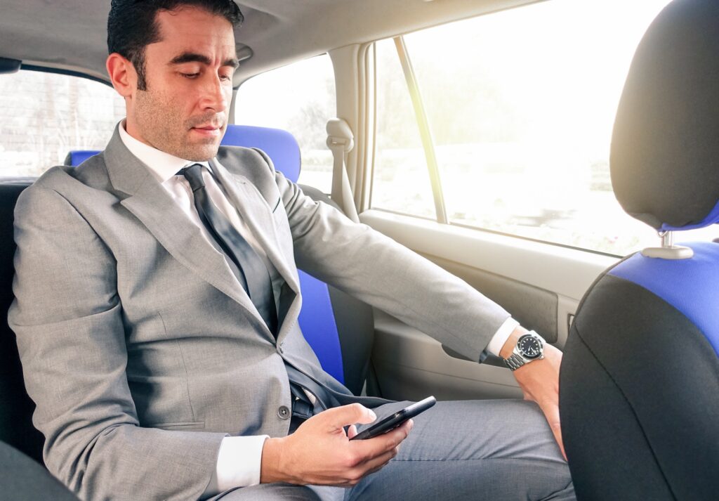 Young handsome businessman sitting in taxi cab using phone
